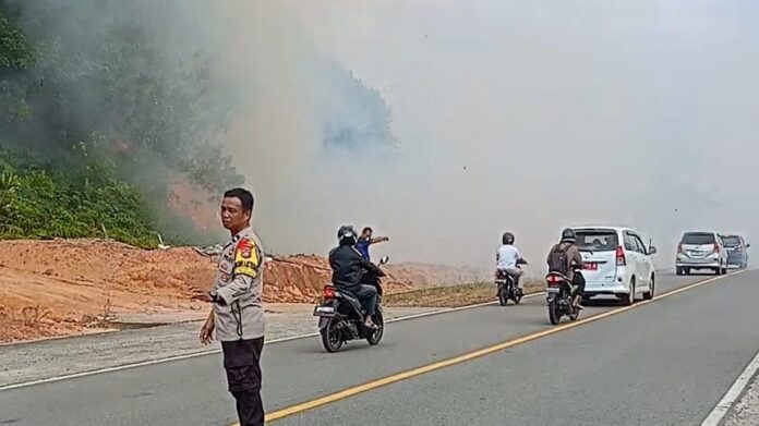 Bhabinkamtibmas Aida Guspa A mengambil inisiatif melakukan pengaturan jalan. Dan mengalihkan kendaraan untuk berbalik arah selama asap tebal menutupi jalan. (Foto : abdi perdana - batamtv.com)